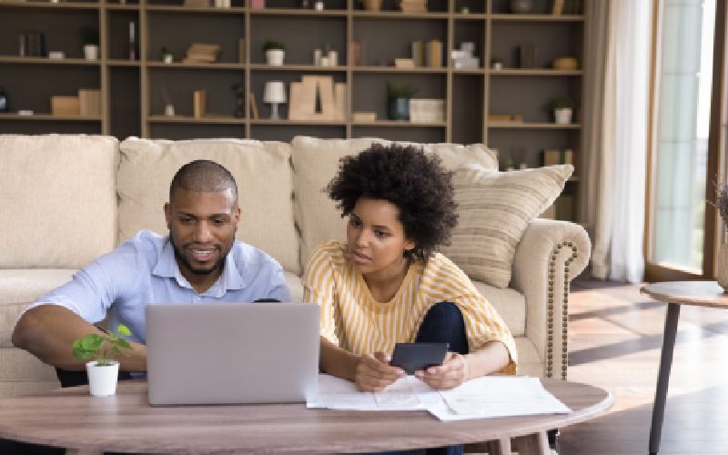 Millennial African American couple using laptop computer at home, making online payments, paying paper bills, insurance, mortgage fees, planning expenses, calculating, money, shopping