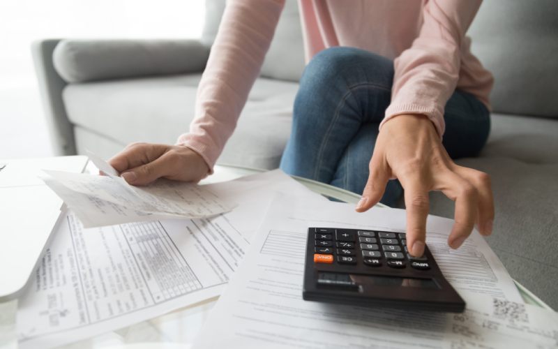 Woman renter holding paper bills using calculator for business financial accounting calculate money bank loan rent payments manage expenses finances taxes doing paperwork concept, close up view