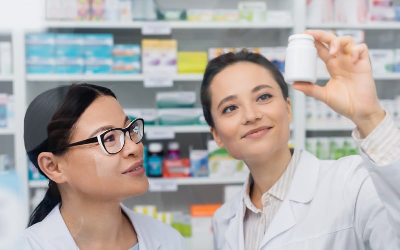 cheerful pharmacist white-coat-holding-bottle asian colleague glasses