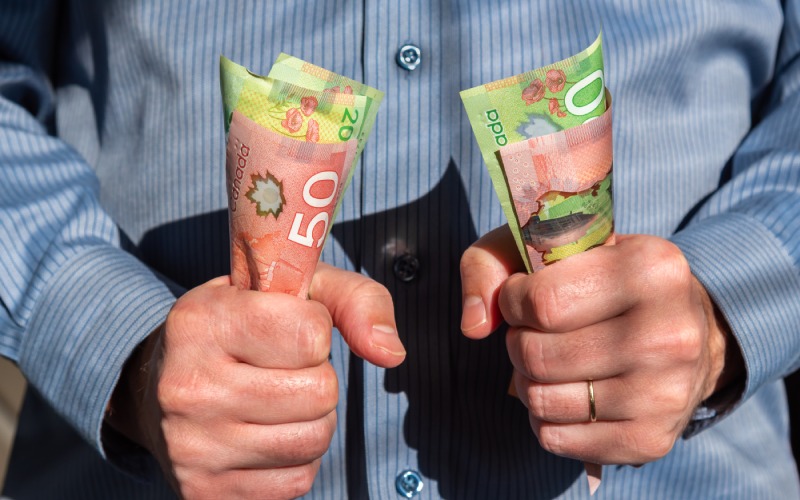 man tightly holding canadian-twenty-fifty dollar bills both hands