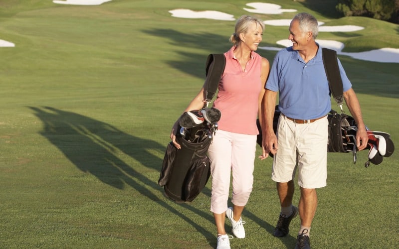 senior couple walking golf course carrying bags