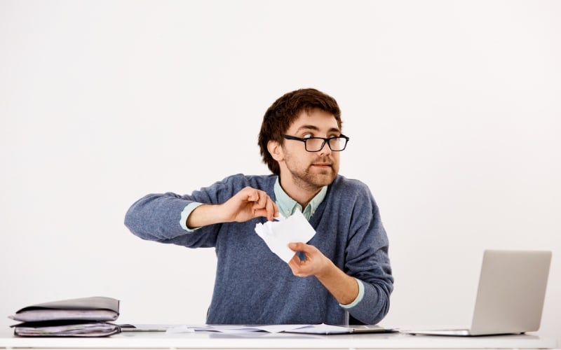 young guy employee acting-crazy-work-sit-office-desk- tearing apart documents